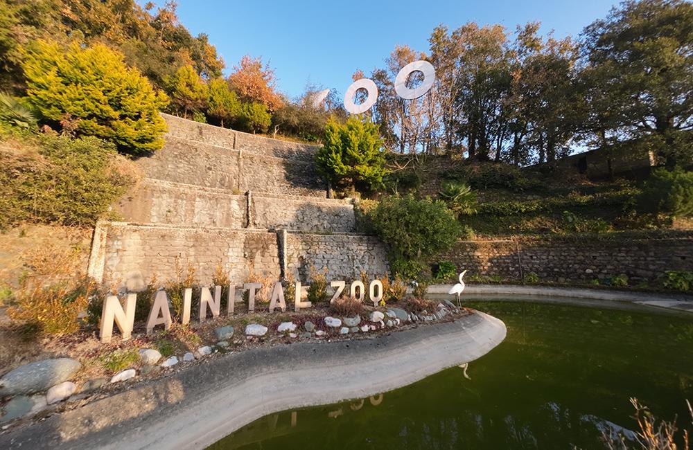 The entrance to the Nainital Zoo, showing a sign with the zoo's name on a tiered stone landscape with a pond.