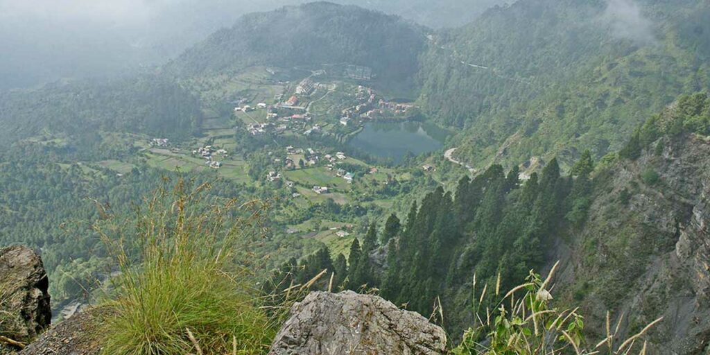  A wide shot from a high cliff viewpoint showing a valley, a lake, and distant hills shrouded in mist.