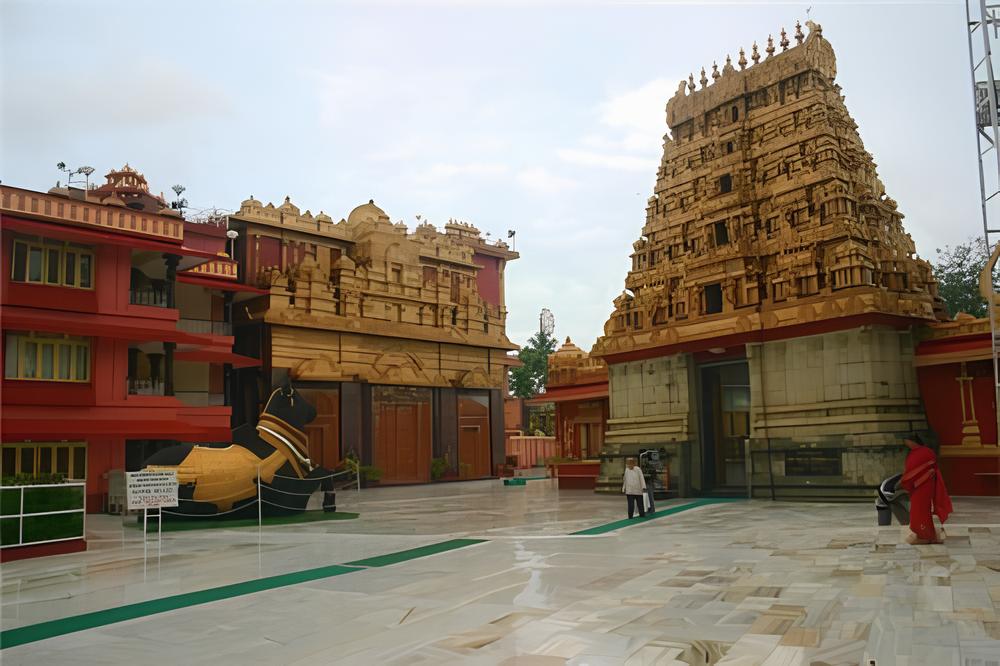 A view of the Mangaladevi Temple complex in Mangalore, showing a large golden gopuram, a statue of a bull, and the temple courtyard.