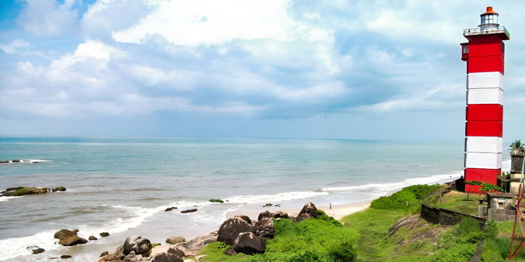 The Surathkal Lighthouse on a rocky coast at sunset, with a path leading towards the tower and the sea.